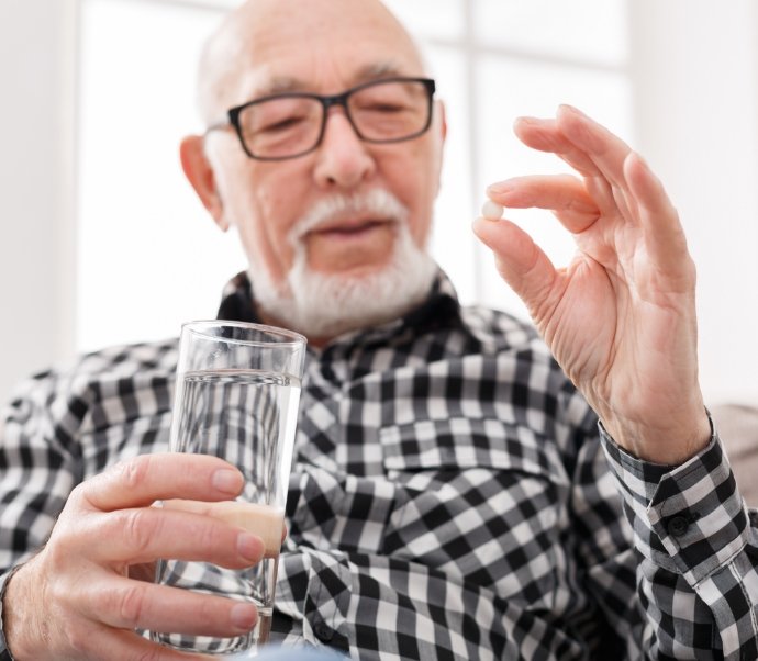 Older man holding pill and glass of water