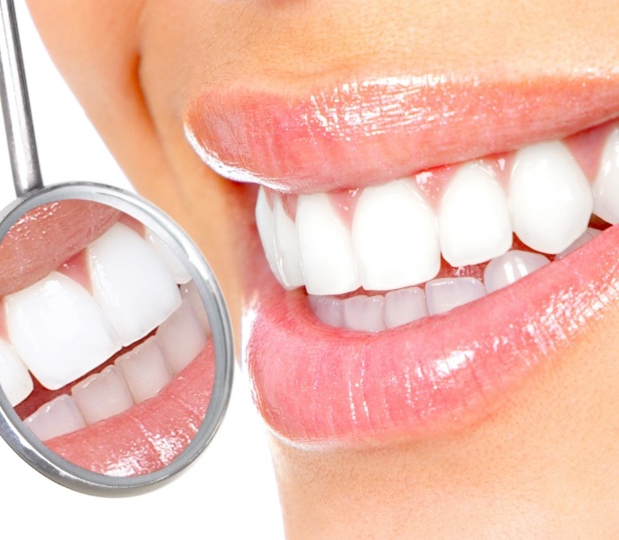 Close up of dental mirror reflecting smile with white teeth