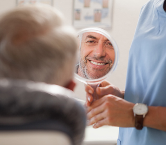 Man smiling at reflection in handheld mirror