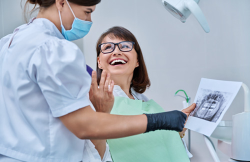 Woman smiling with dentist while reviewing X-ray