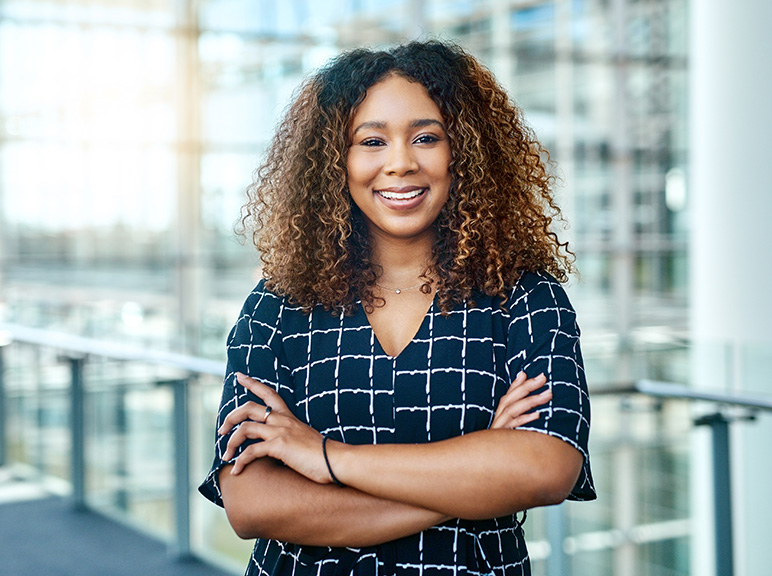 Benefit Image Nine Smiling woman with curly hair standing confidently in a modern office building.