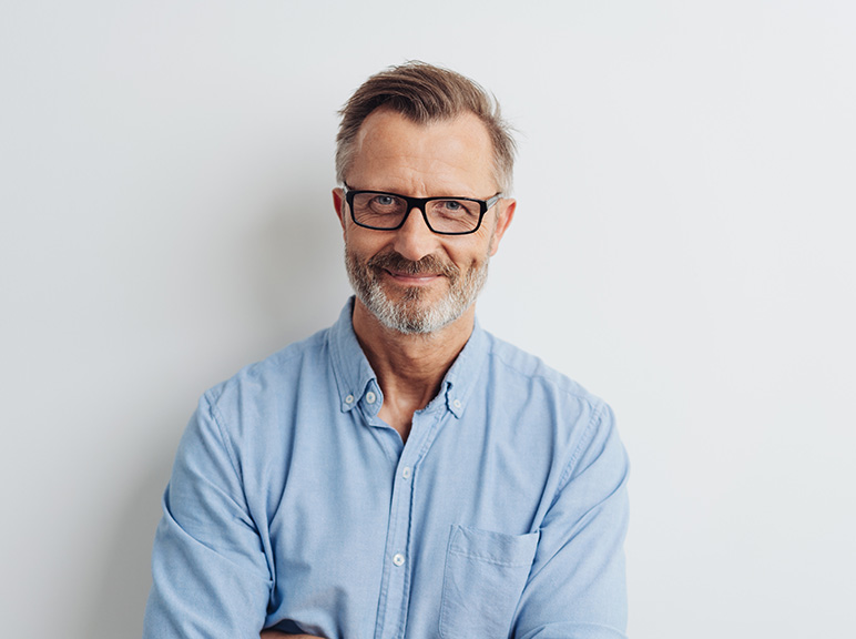 Middle-aged man with glasses and beard smiling against a plain background.