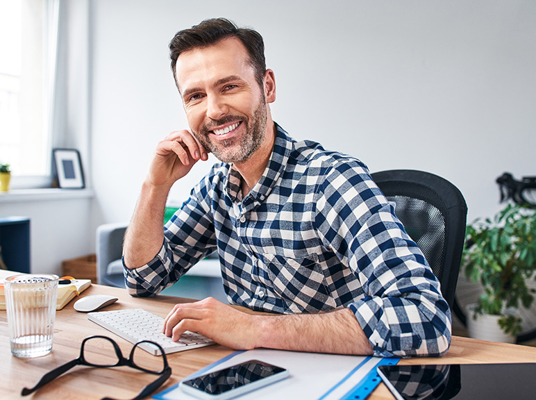 Benefit Image Two Smiling man working at a desk with computer, phone, and office supplies.