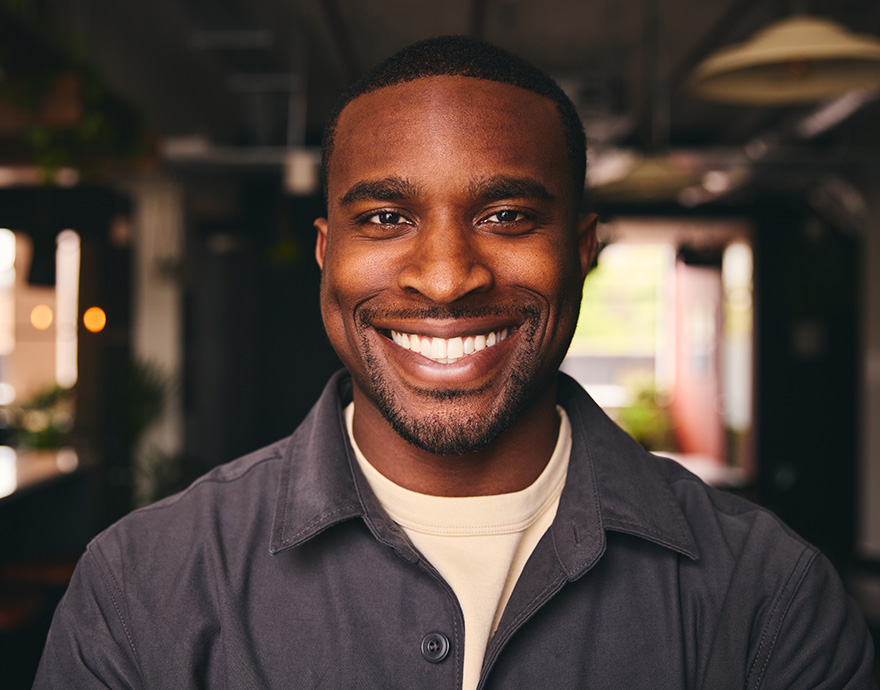 Services Image Three Close-up portrait of a smiling man in a dark jacket with a softly lit indoor background.